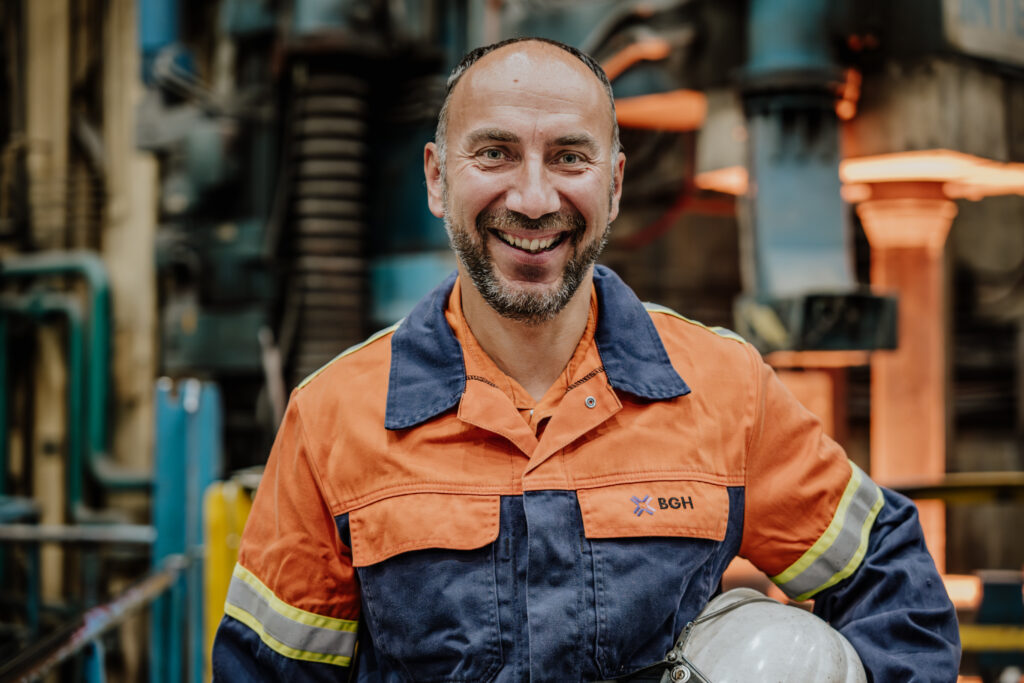 Lächelnder Industriearbeiter in Schutzkleidung vor Maschinen – professionelle Business- und Industriefotografie von Yourfilms.