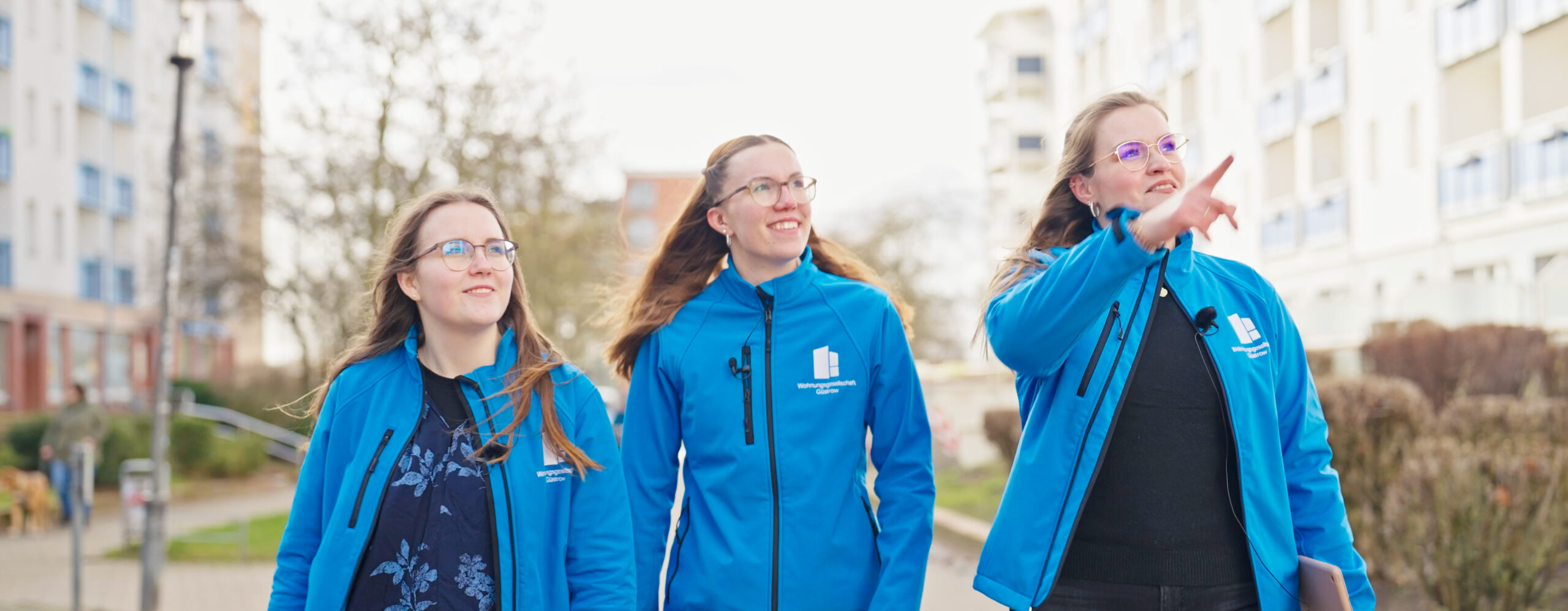 Drei Mitarbeiterinnen der Wohnungsgesellschaft Güstrow in blauen Arbeitsjacken, unterwegs in einer modernen städtischen Umgebung – fotografiert von Yourfilms.